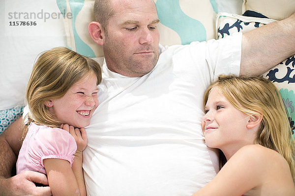 Draufsicht eines reifen Mannes zwischen zwei Töchtern auf dem Bett