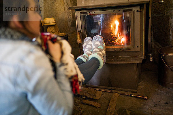 Junge Frau wärmt die Füße vor dem Feuer