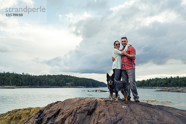 Porträt eines romantischen Paares mittlerer Erwachsener und eines Hundes auf einem Felsen an der Küste von Maine  USA