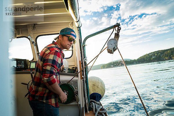 Junger Mann hebt Winde auf Fischerboot an der Küste von Maine  USA