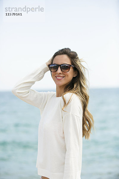 Hübsche blonde Frau mit Sonnenbrille am Strand  lächelnd vor der Kamera.