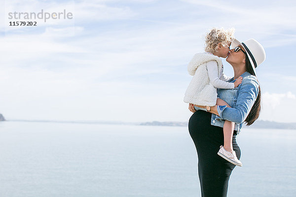 Schwangere Mutter küsst Tochter an der Küste