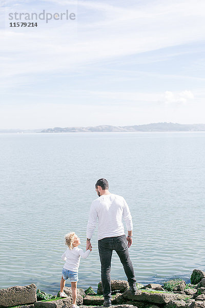 Rückansicht eines reifen Mannes und einer Tochter an der Wasserkante an der Küste