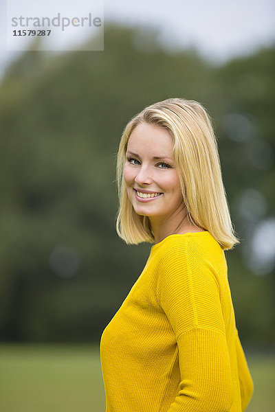 Porträt einer hübschen blonden Frau im Park  die vor der Kamera lächelt.