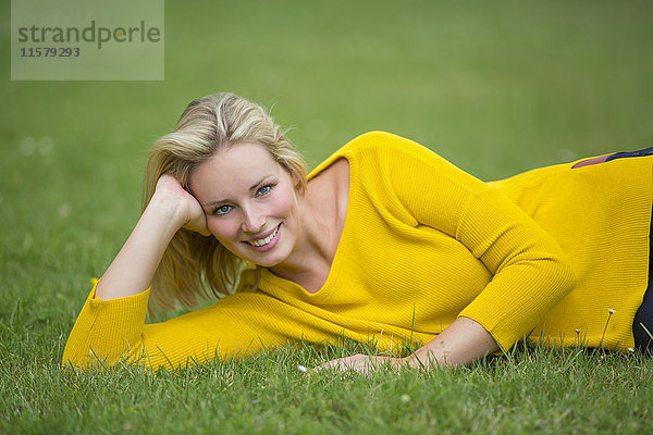 Porträt einer hübschen blonden Frau  die im Park liegt und vor der Kamera lächelt.