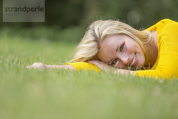 Porträt einer hübschen blonden Frau  die im Park liegt und vor der Kamera lächelt.