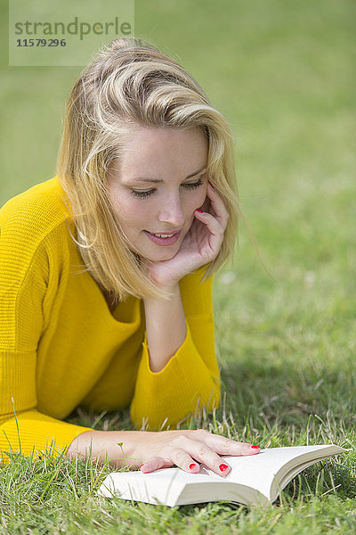 Blonde hübsche Frau beim Lesen eines Buches im Park