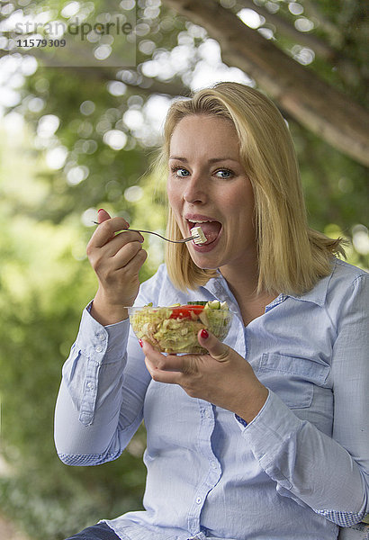 Hübsche blonde Frau  die einen Salat im Park genießt.