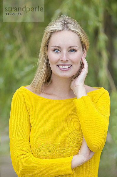 Porträt einer blonden Frau im Park lächelnd vor der Kamera