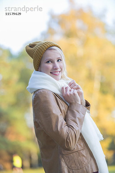 Porträt einer zufriedenen hübschen blonden Frau mit Mütze und Schal im Herbst