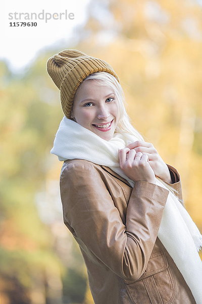 Porträt einer zufriedenen hübschen blonden Frau mit Haube und Schal im Herbst lächelnd vor der Kamera