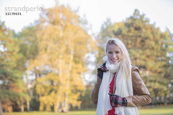 Portrait einer zufriedenen hübschen blonden Frau mit Handschuhen und Schal im Herbst lächelnd vor der Kamera