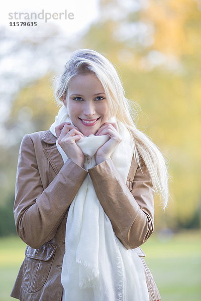 Porträt einer zufriedenen hübschen blonden Frau mit Schal im Herbst lächelnd vor der Kamera