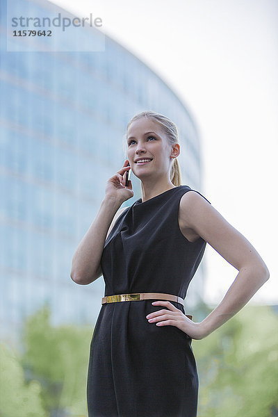 Portrait einer Geschäftsfrau mit Handy vor einem Bürogebäude