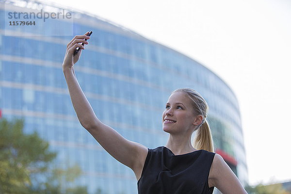 Hübsche junge Frau  die einen Selfie vor einem Bürogebäude nimmt.