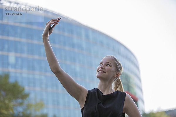 Hübsche junge Frau  die einen Selfie vor einem Bürogebäude nimmt.