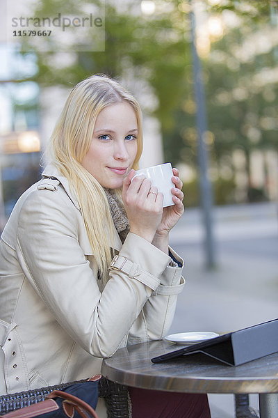 Hübsche blonde Frau genießt eine Tasse Kaffee in der Innenstadt mit Blick auf die Kamera.