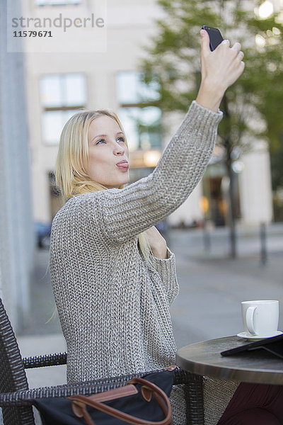 Verspielte hübsche junge Frau bei einem Selfie in einem Cafe im Stadtzentrum