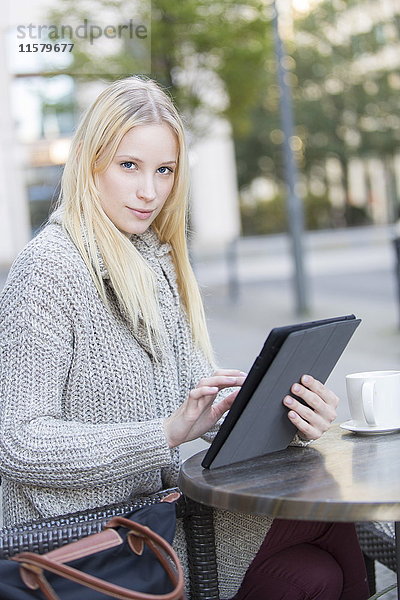 Hübsche junge Frau mit Tablette in einem Cafe im Stadtzentrum mit Blick auf die Kamera