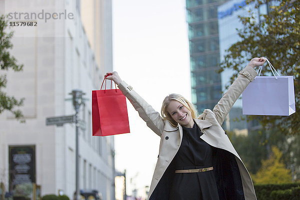 Hübsche blonde Frau mit erhobenen Armen und Einkaufstaschen in der Innenstadt.
