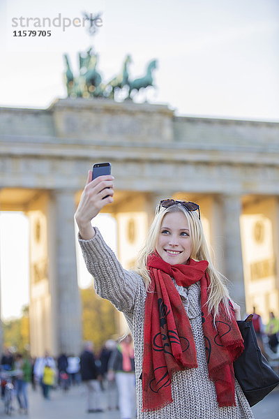 Hübsche blonde Frau mit einem Selfie vor dem Brandenburger Tor in Berlin.