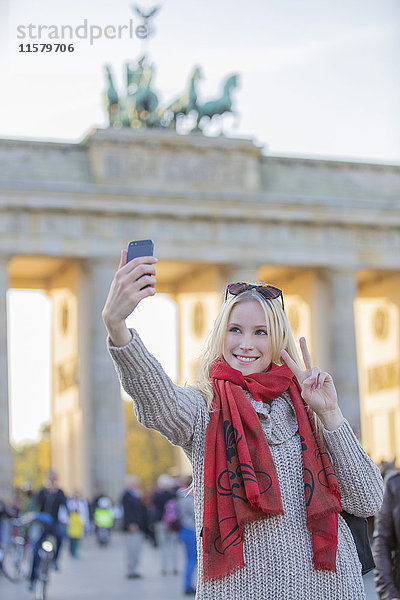 Hübsche blonde Frau beim Selfie vor dem Brandenburger Tor in Berlin.