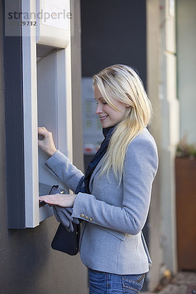 Hübsche blonde Frau an einem Geldautomaten.