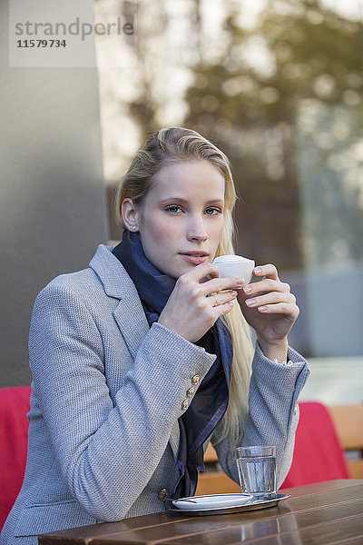 Hübsche blonde Frau genießt eine Tasse Kaffee in einem Café und schaut in die Kamera.