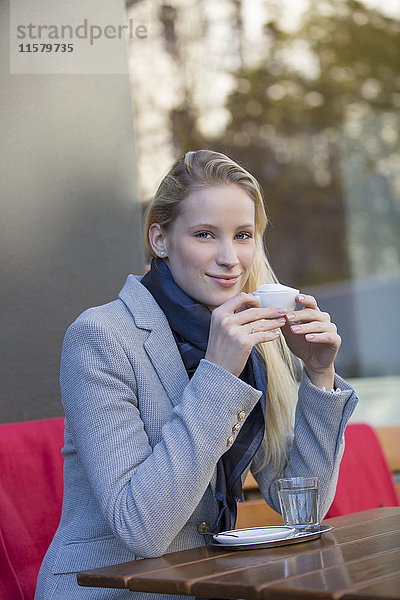 Hübsche blonde Frau genießt eine Tasse Kaffee in einem Cafe und lächelt in die Kamera.