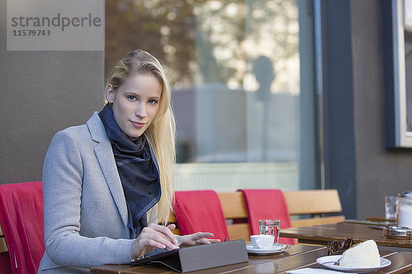 Hübsche blonde Frau mit Tablette in einem Cafe mit Blick auf die Kamera
