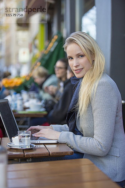 Hübsche blonde Frau mit Laptop in einem Cafe lächelnd vor der Kamera