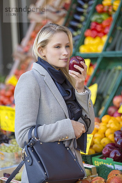 Hübsche blonde Frau  die auf dem Markt gesundes Essen kauft und Apfel riecht.