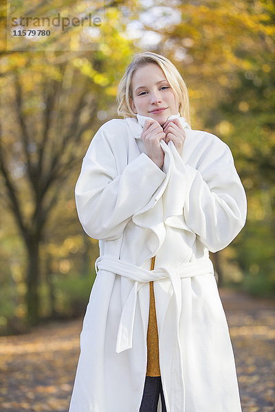 Porträt einer hübschen blonden Frau mit Mantel im Park im Herbst