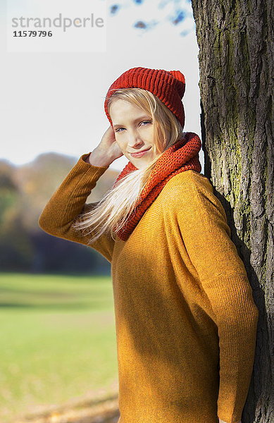 Blonde Frau lehnt sich im Herbst an einen Baum im Park.