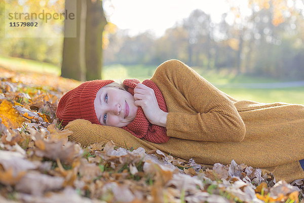 Nachdenkliche blonde Frau  die im Herbst im Park liegt.