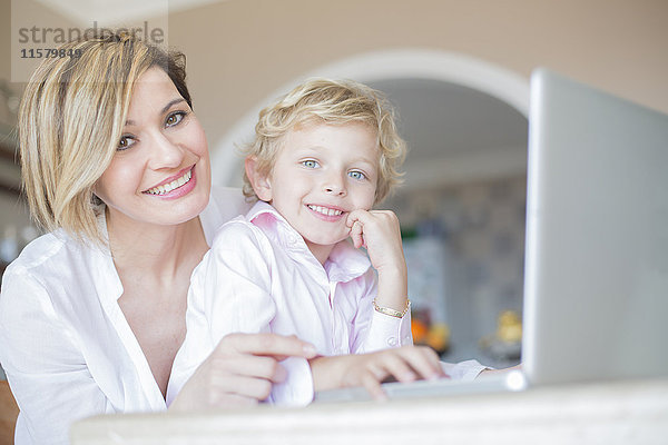 Mutter und Sohn mit Laptop zu Hause lächelnd vor der Kamera
