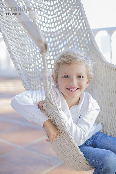 Porträt eines süßen Jungen in einer Hängematte im Freien lächelnd vor der Kamera