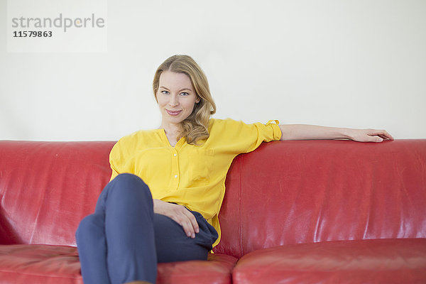 Porträt einer hübschen blonden Frau auf der Couch mit Blick auf die Kamera