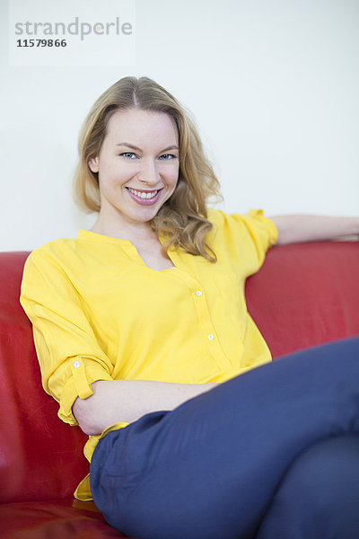 Porträt einer hübschen blonden Frau auf der Couch  die vor der Kamera lächelt.