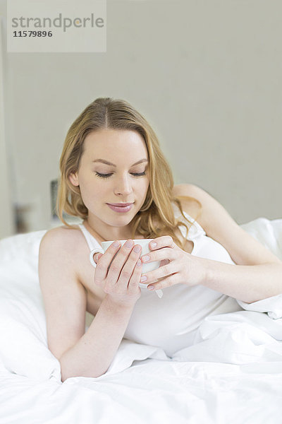 Hübsche blonde Frau  die einen Tee im Bett genießt.