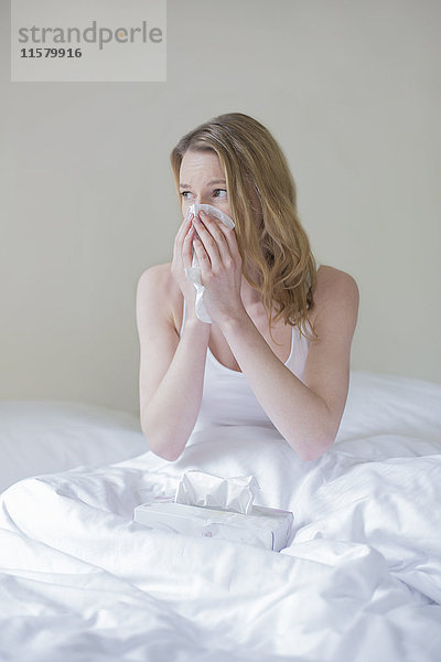 Frau krank mit Taschentüchern im Bett