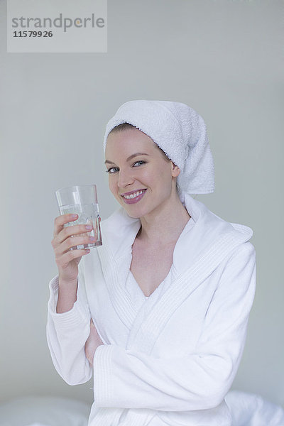 Frau im Bademantel mit einem Glas Wasser lächelnd vor der Kamera