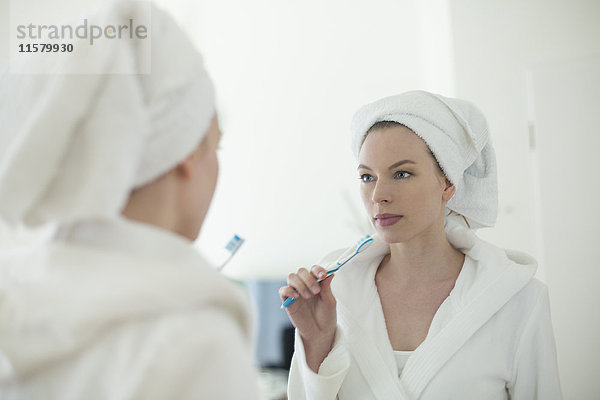 Frau im Bademantel beim Zähneputzen vor dem Spiegel