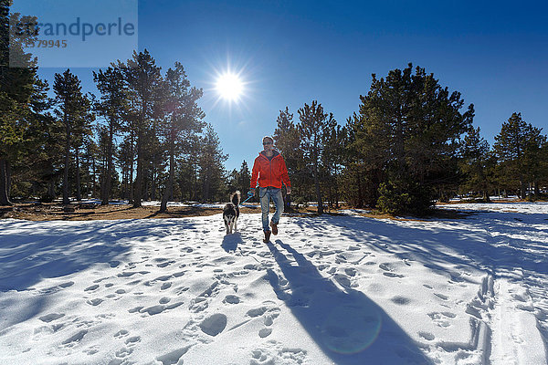 Ausgewachsener Mann geht mit Hund im verschneiten Wald spazieren