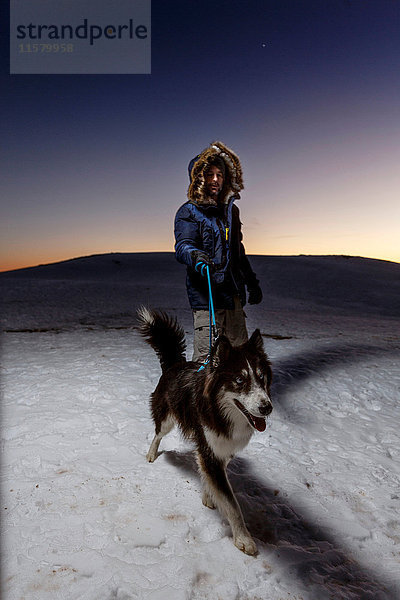 Erwachsener Mann geht nachts mit Hund im Schnee spazieren