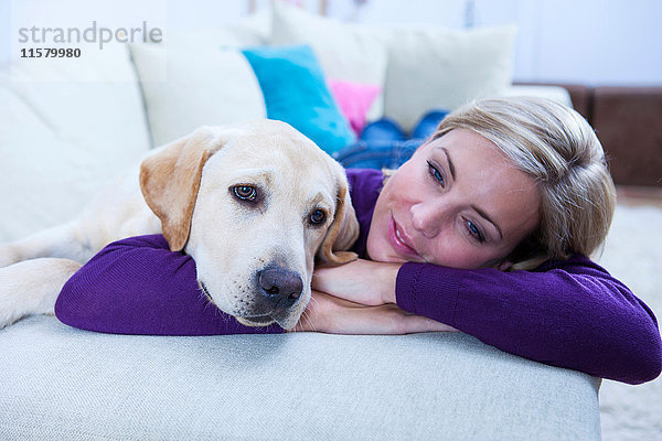 Mittlere erwachsene Frau  die mit ihrem Labradorhund auf dem Sofa liegt