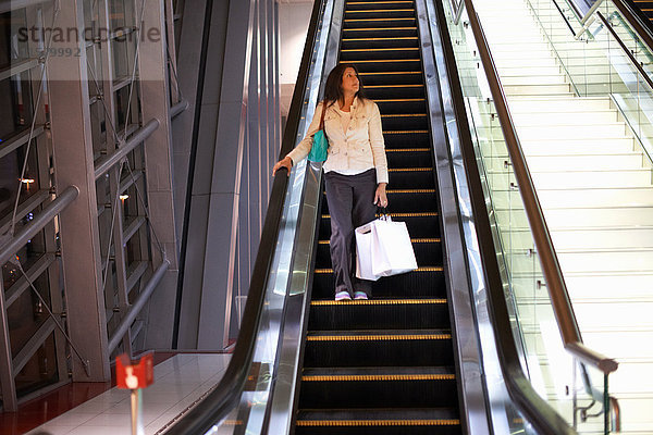 Reife Frau mit Einkaufstüten  die sich auf der Rolltreppe in einem Einkaufszentrum nach unten bewegen  Dubai  Vereinigte Arabische Emirate