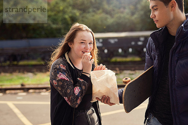 Junger Mann teilt eine Tüte Chips mit einer jungen Frau  Skateboard unter dem Arm eines jungen Mannes  Bristol  UK