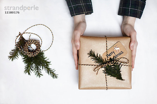 Frau hält Weihnachtsgeschenk  in braunes Papier eingewickelt  mit Farn und Schnur dekoriert  Draufsicht