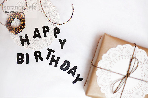 Geschenk verpackt in braunes Papier  Deckchen und Schnur  daneben Buchstaben mit der Aufschrift Happy Birthday